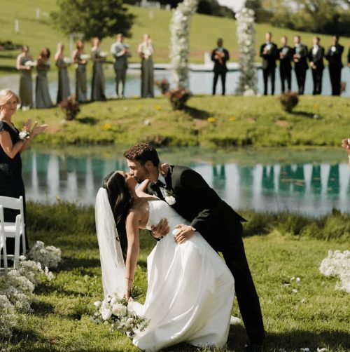 Ceremonia junto al lago con sillas blancas en Cedar Pond Farms