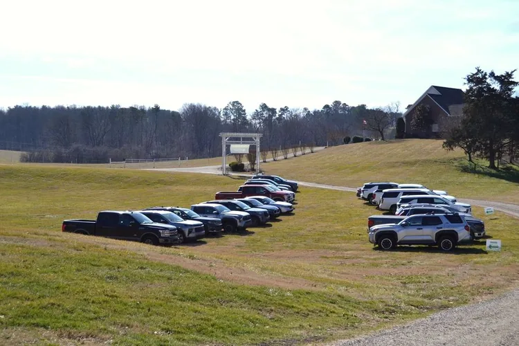 Guest cars parked in the meadow below the rolling hills of East Tennessee during a company event.