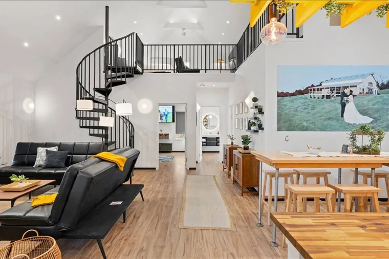 Climb the spiral staircase to the loft in this three-bedroom barndominium great room at the fluffy cow farm — leather sofas below and long farm tables ready for your group.