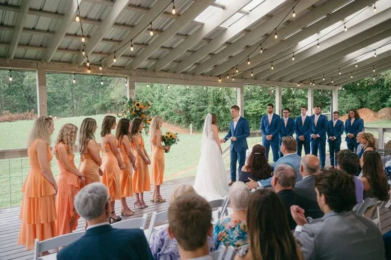 Una ceremonia de boda bajo la Grand Veranda techada con luces de bistró y vistas de la granja
