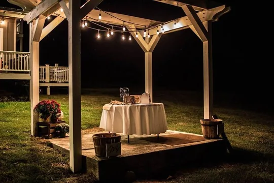 El arco del Escenario Principal iluminado con luces de cadena de noche, con escalones curvos, en Cedar Pond Farms