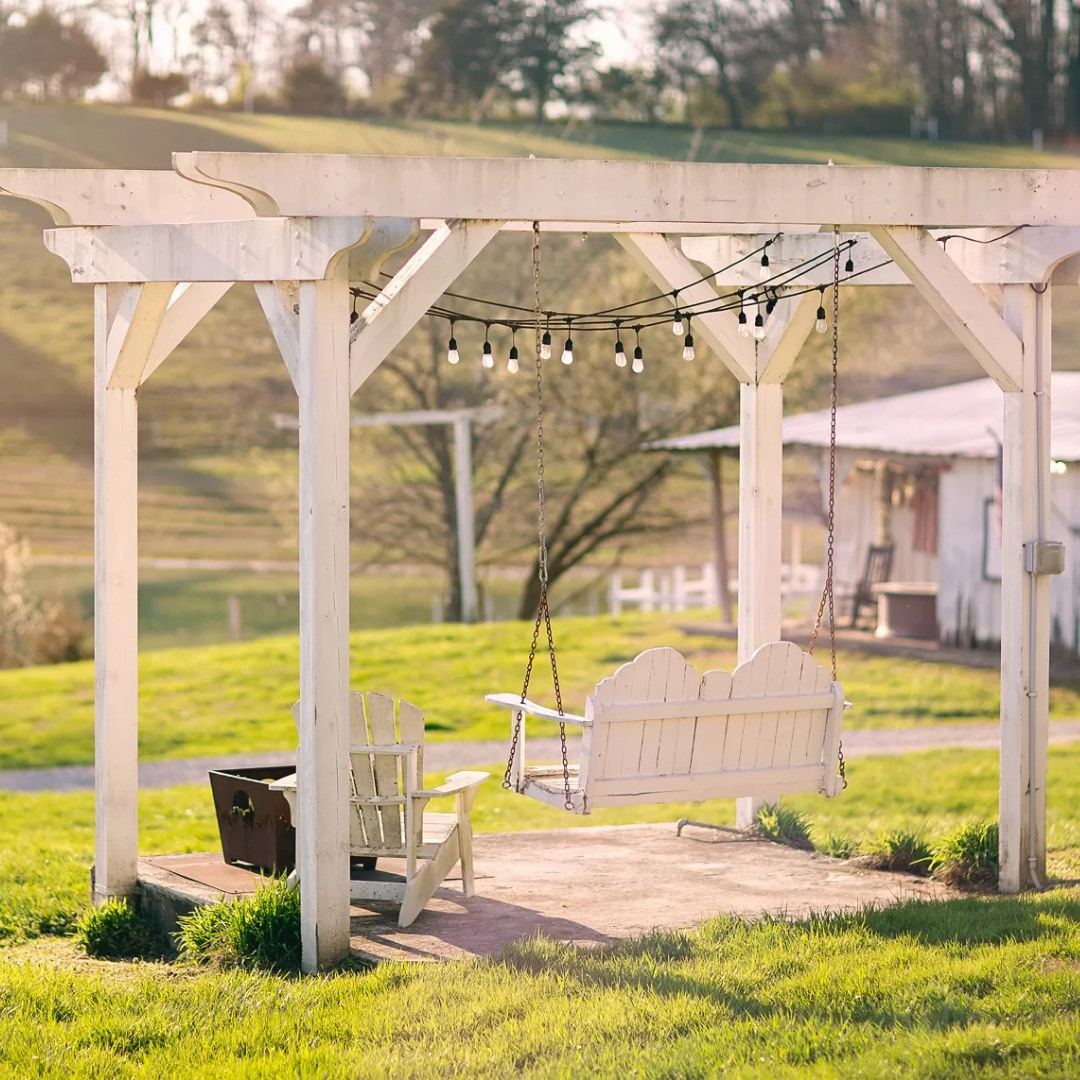 A white Pond Side Swing Arbor with porch swing and string lights at golden hour