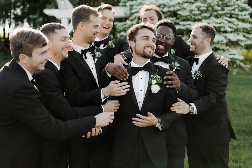 Groomsmen laughing together beside the pond ceremony arbor at an intimate farm wedding in New Market, Tennessee